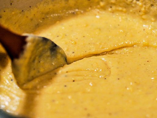 Closeup of simmering polenta being stirred with a wooden spoon.