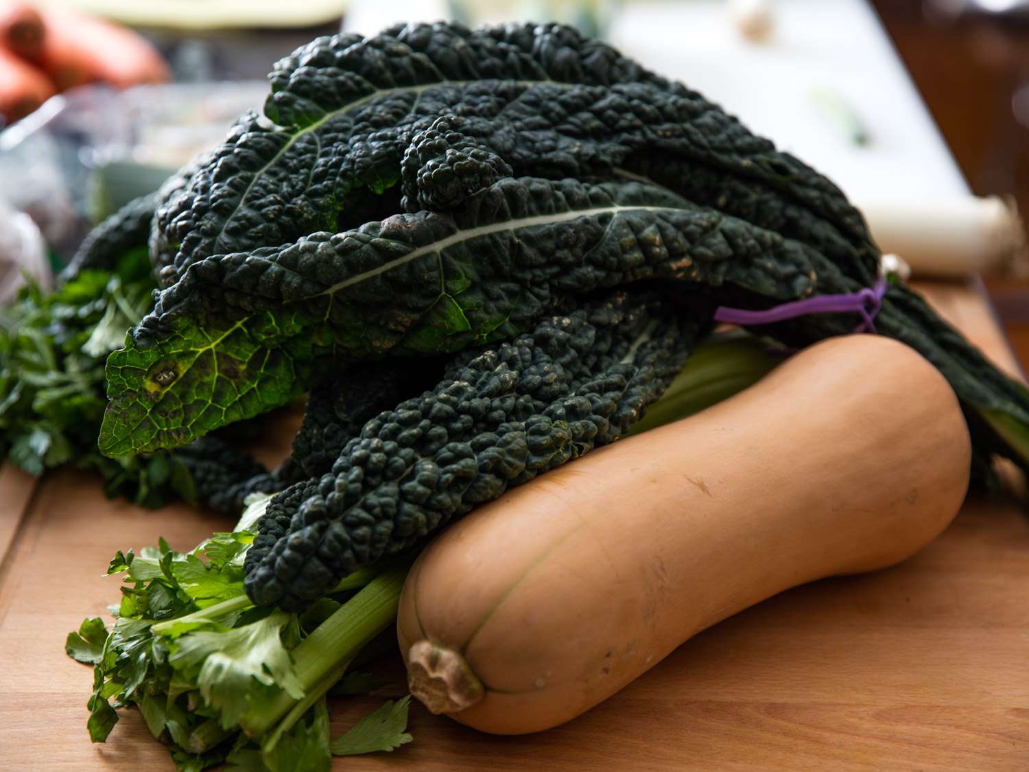 A bunch of lacinato kale, a bunch of celery, and a slender butternut squash sitting on a cutting board.