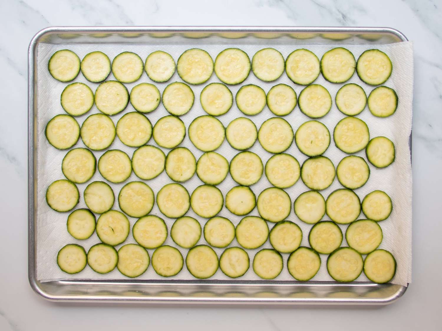 Macerated zucchini slices placed on a paper towel in a rimmed baking sheet to drain