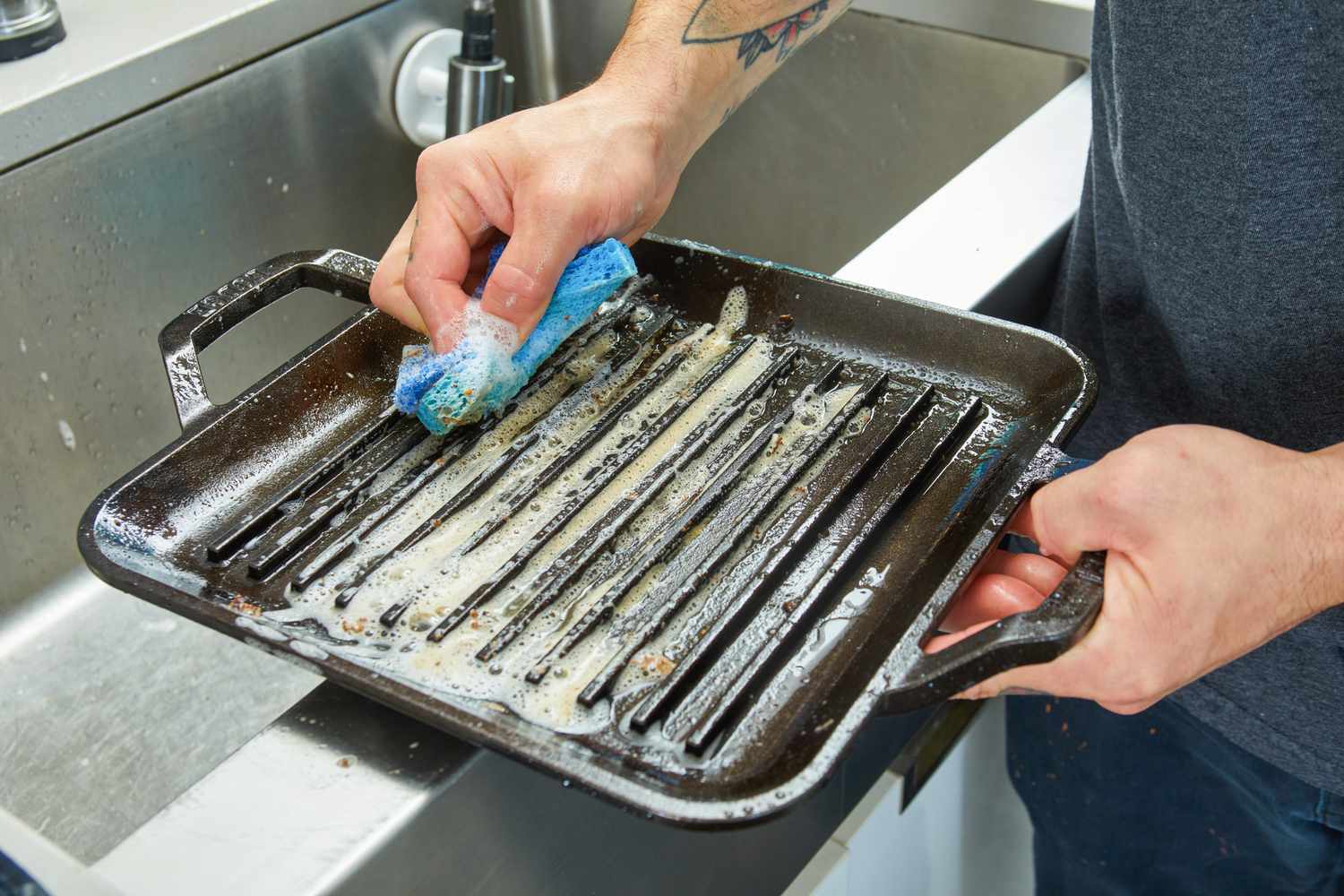 A person cleaning the Lodge 11-Inch Cast Iron Square Grill Pan with soap and water 