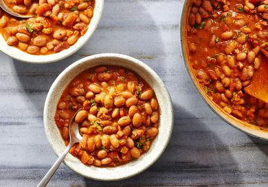 Two bowls and a pot of frijoles charros, on a stone background.