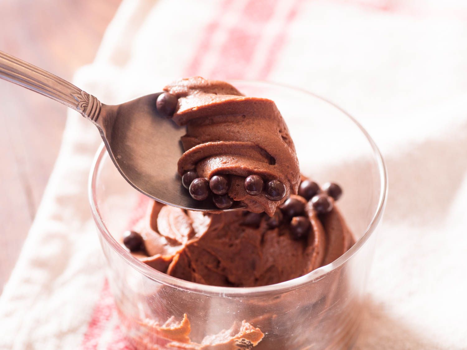 A spoonful of eggless chocolate mousse being lifted from a dessert glass.