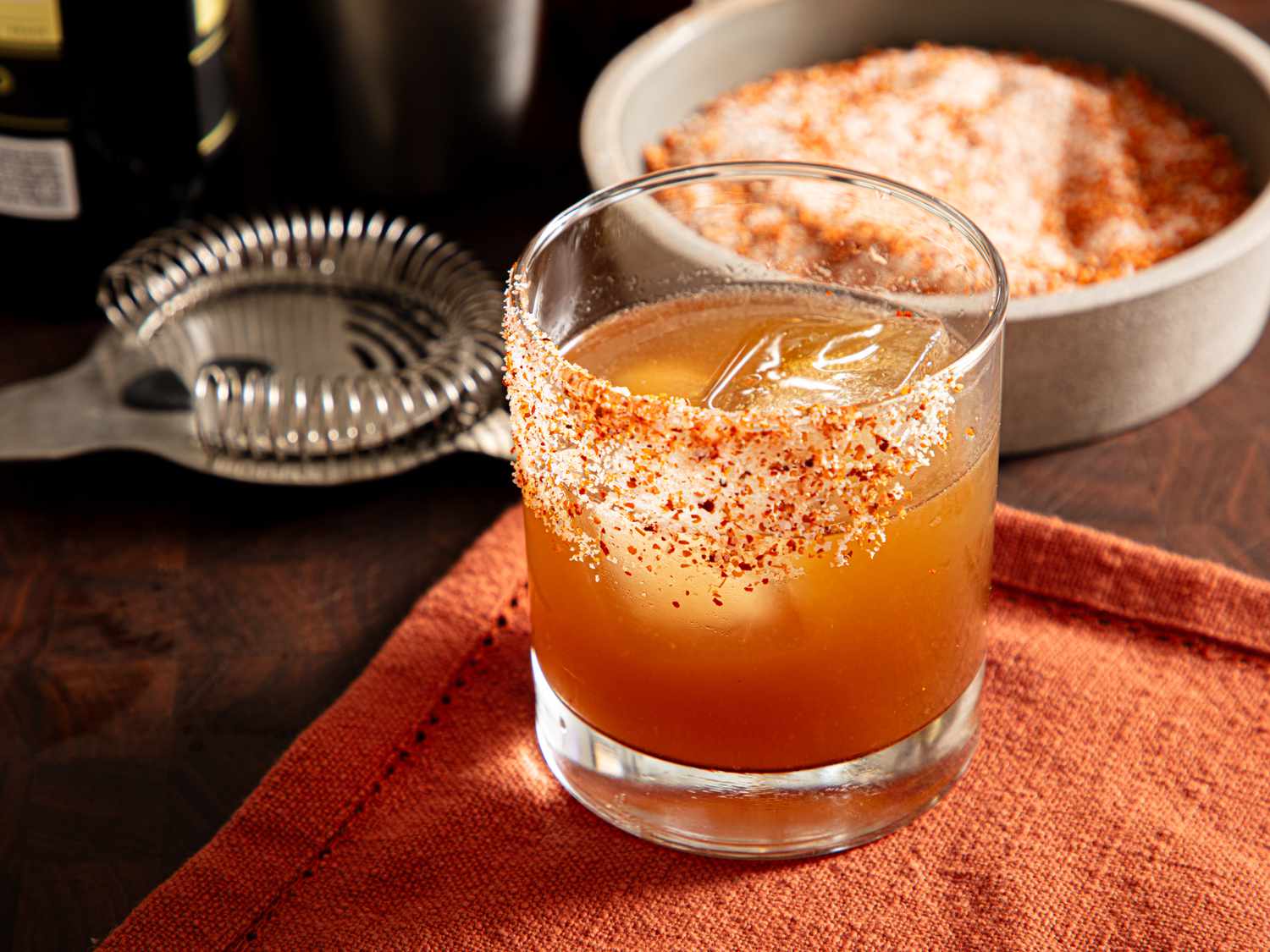 A prepared margarita cocktail with a spicy rim garnish placed on an orange napkin