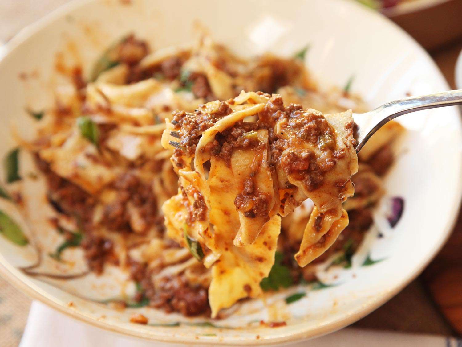 Close-up of a forkful of tagliatelle, coated with ragù Bolognese.