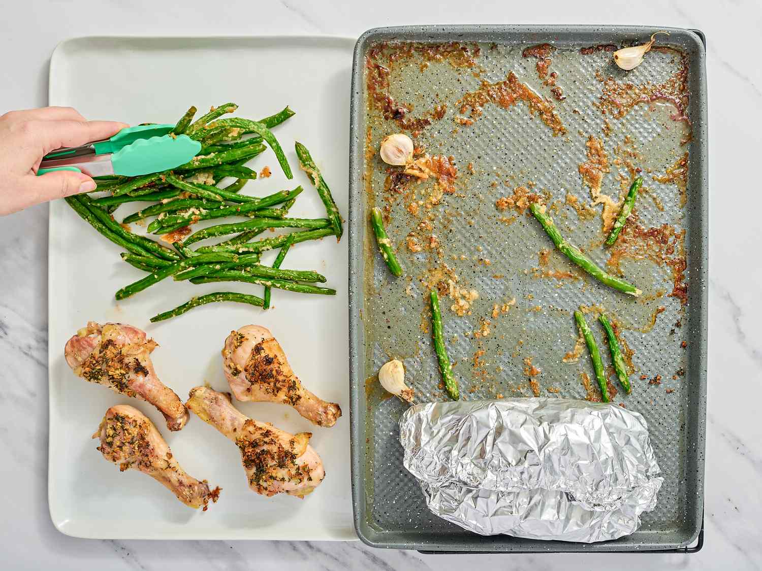 Green beans and seasoned chicken drumsticks being prepared on a tray with kitchen tongs