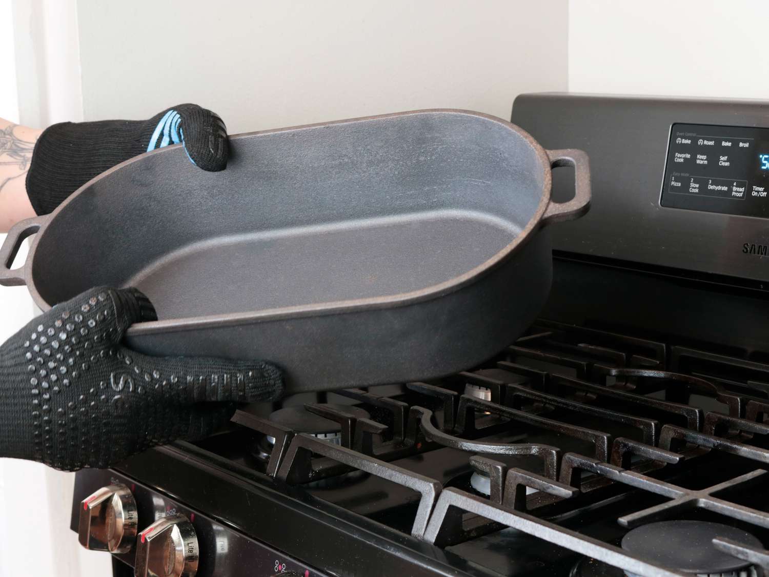 a hot cast iron pan held by two hands in heat resistant grill gloves