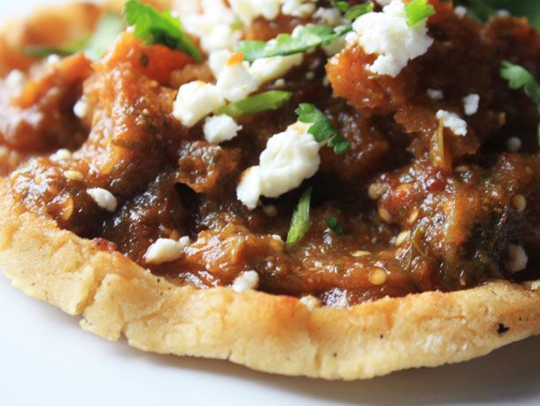 Chicharrones guisados on a sopes, garnished with cilantro and queso fresco.
