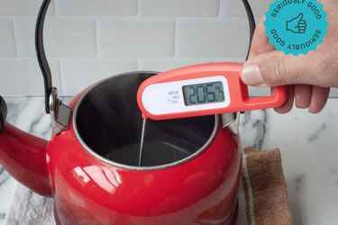 a person holding the lavatools javelin thermometer to measure the temperature of hot water in a tea kettle