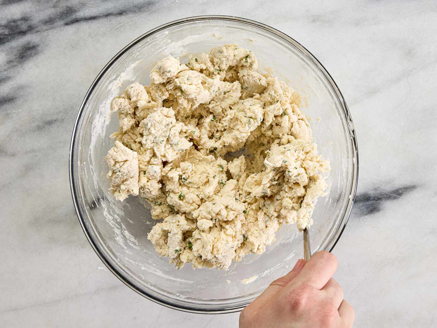 stirring sour cream mixture into dough with a fork in a glass bowl 
