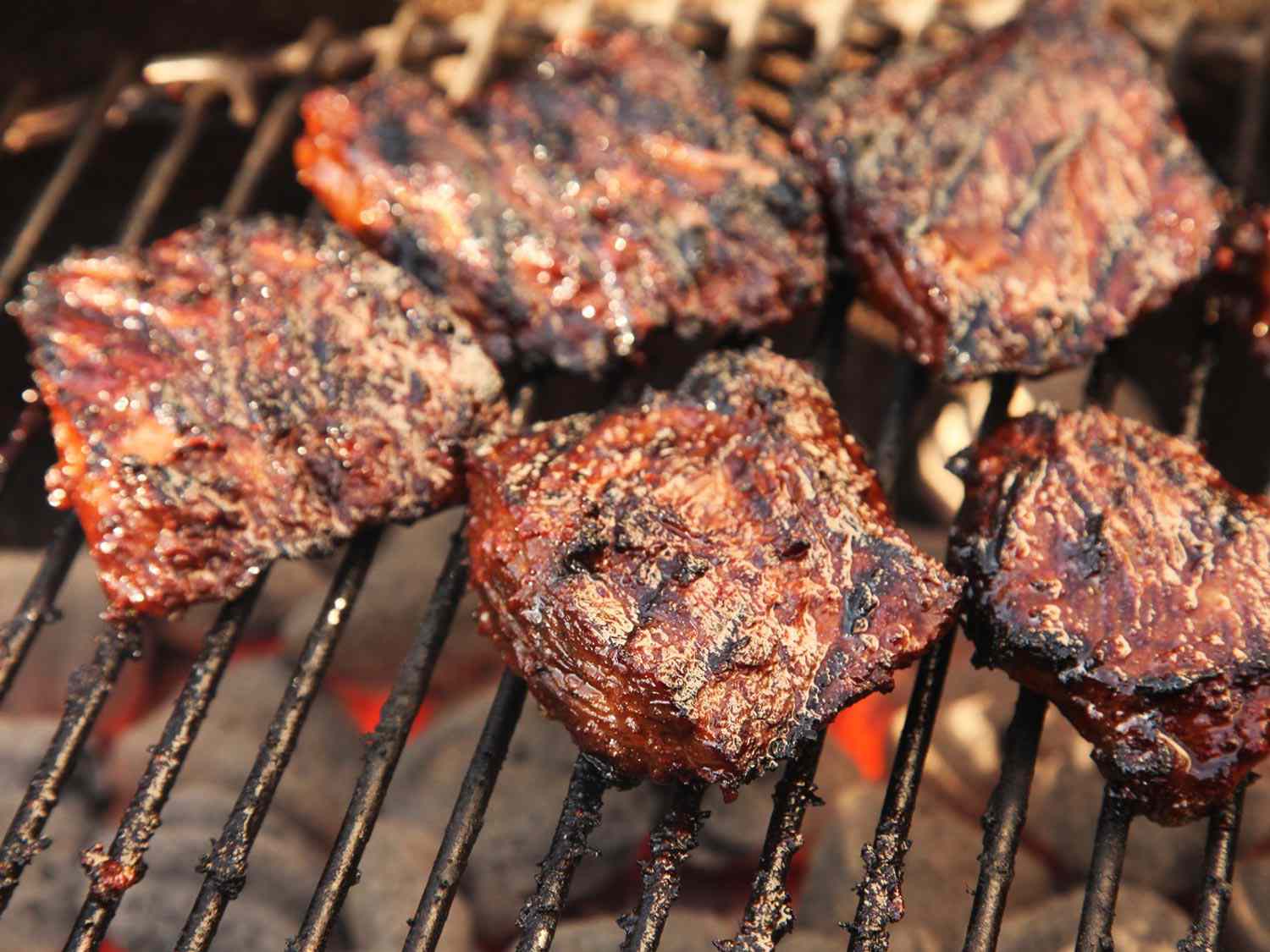 Marinated skirt steaks grilling over charcoal to make carne asada.