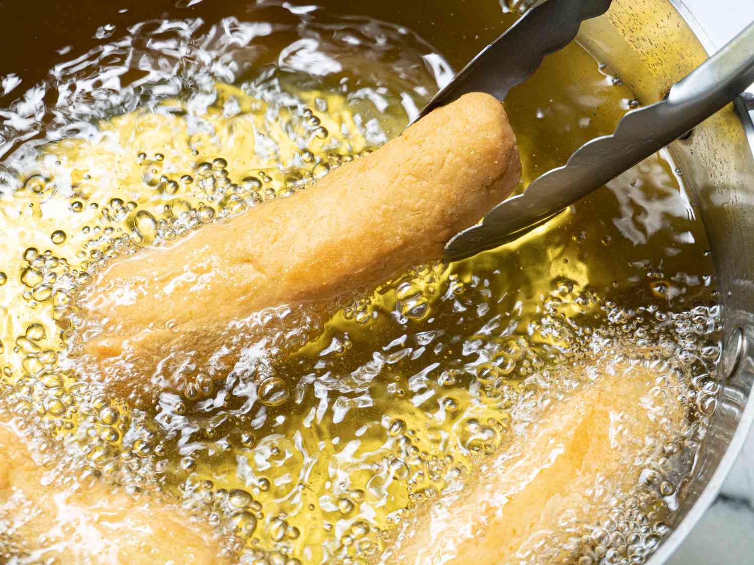 Side angle view of adding dough to oil 