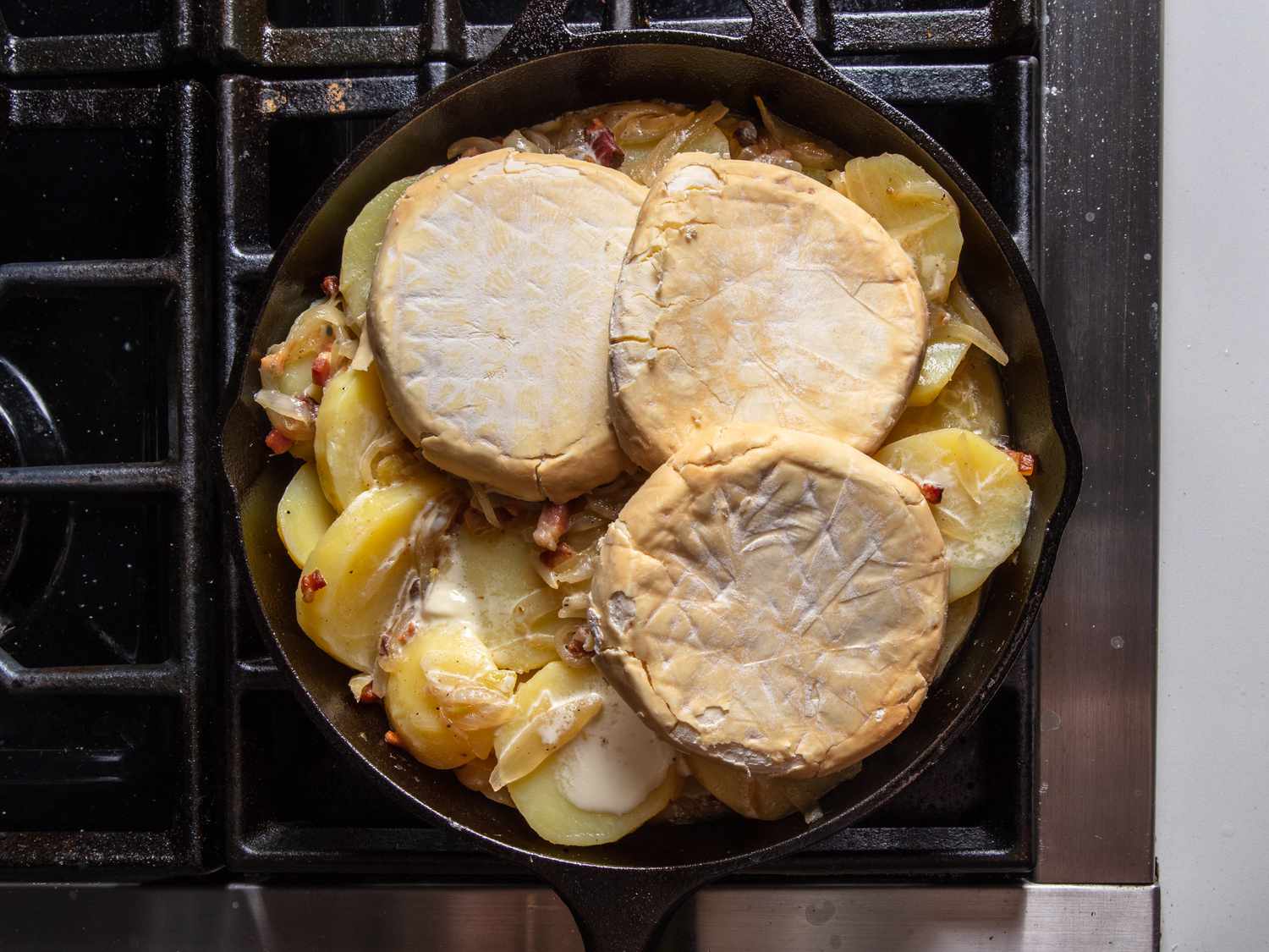 Rounds of soft-rind cheese, each cut in half through the middle, are arranged on top of the potatoes.