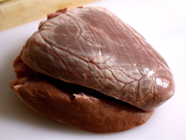 An uncooked beef heart on a white cutting board.