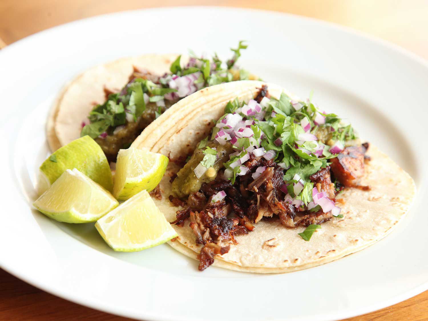 Carnitas tacos on a plate with lime wedges. 
