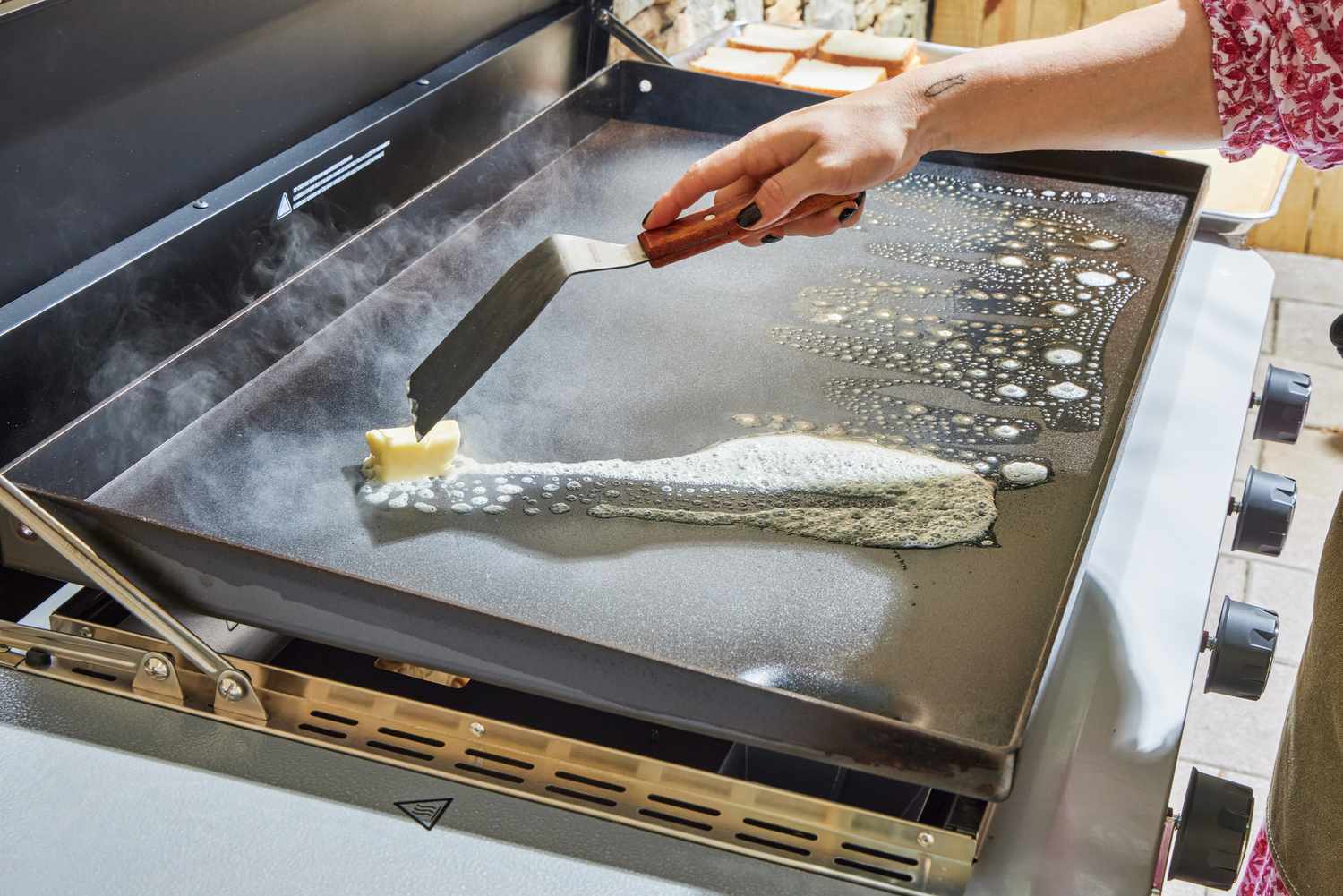 A person melts butter on the Weber 36 Inch Gas Griddle
