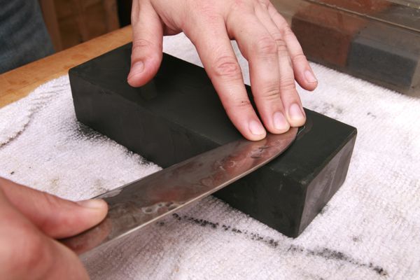 Hands sharpening a knife on a lower grit whetstone