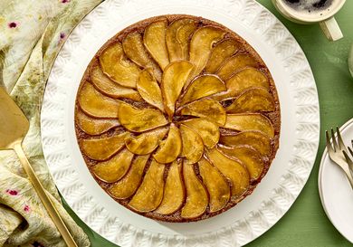 Upsidedown pear cake arranged on a white plate accompanied by tableware and a cup of coffee
