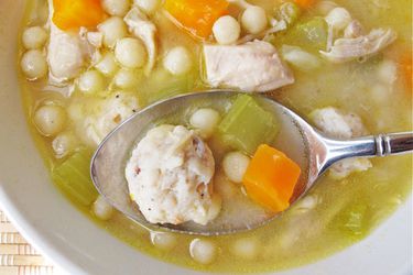 Overhead closeup of a spoon holding up a bite of homemade chickarina soup directly above the bowl.