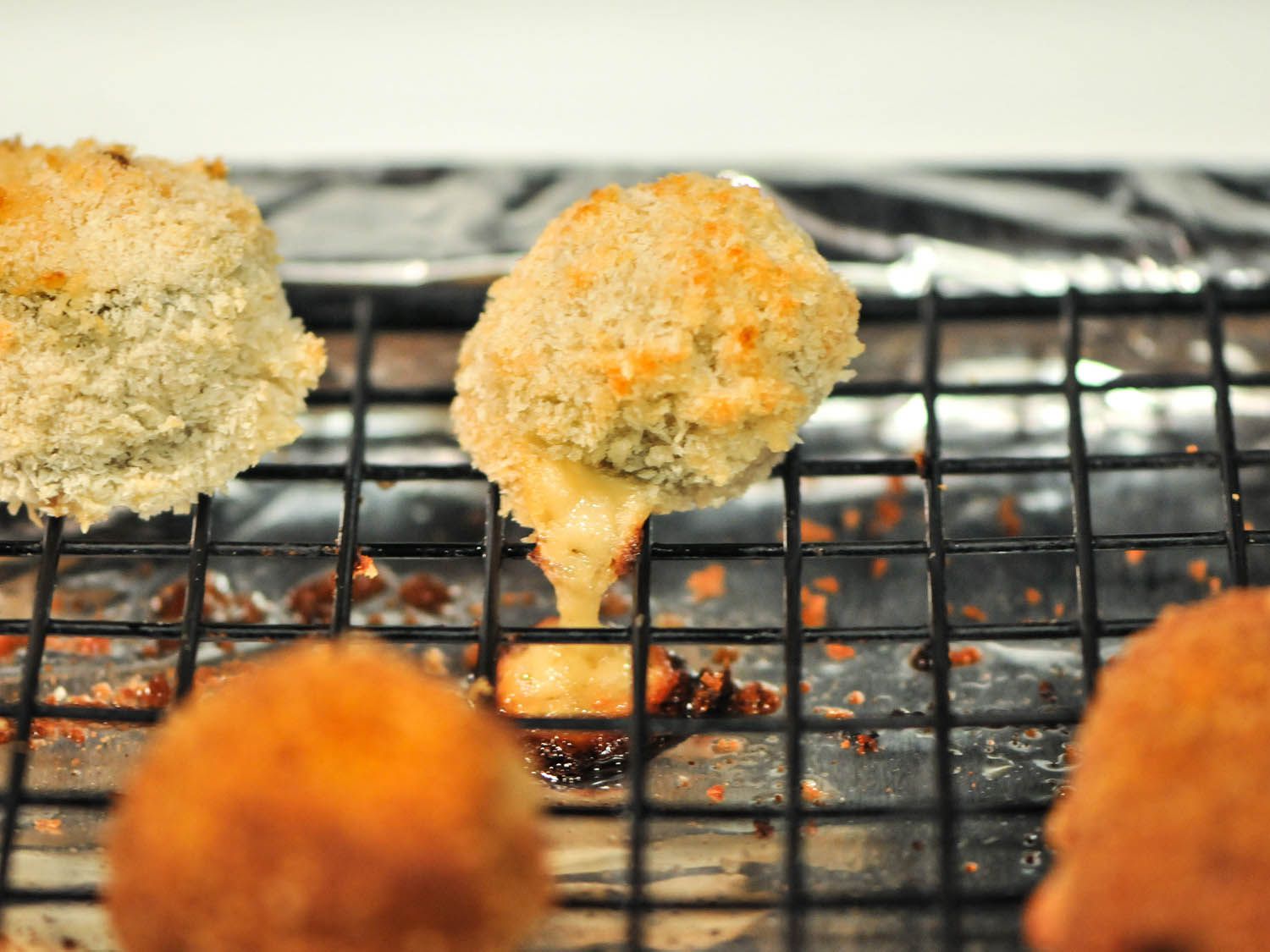 Cheese oozing out from a jalapeno poppers resting on a wire rack in a rimmed baking sheet. 