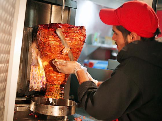 Taquero slicing pastor taco meat from a trompo