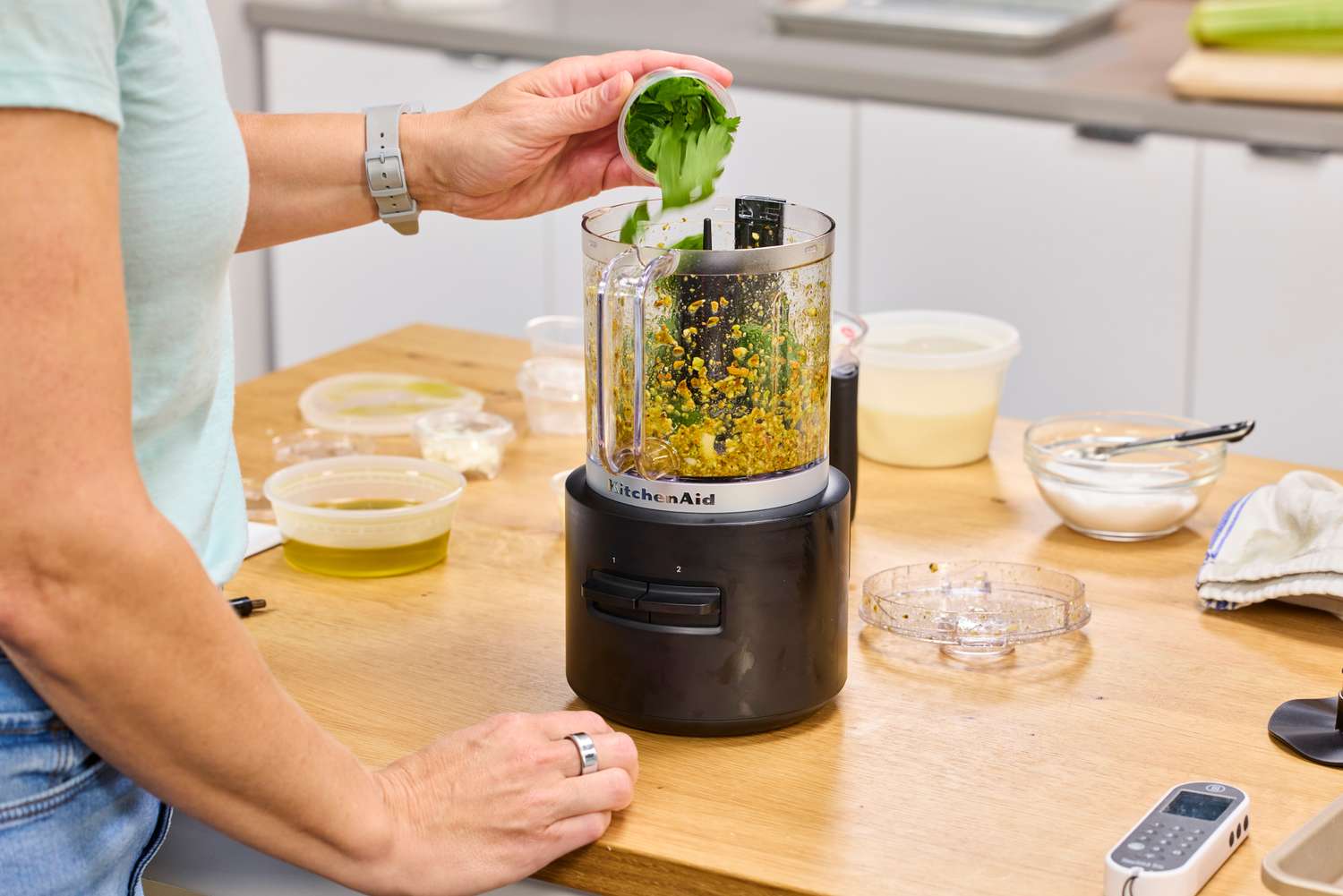 A person adds herbs to the KitchenAid Go Cordless 5-Cup Food Chopper