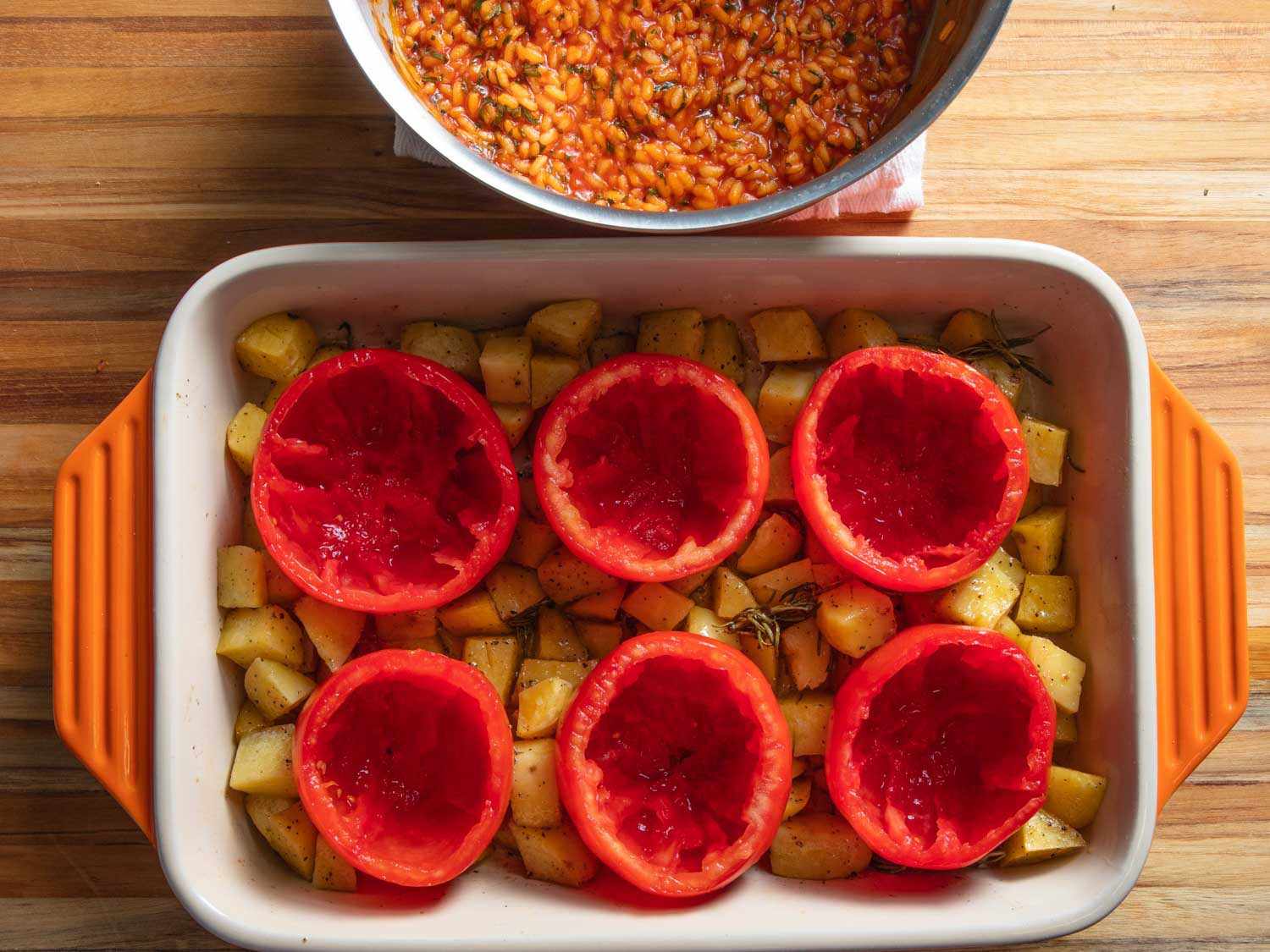 Overhead of hollowed-out tomatoes nestled in a baking dish with potatoes.