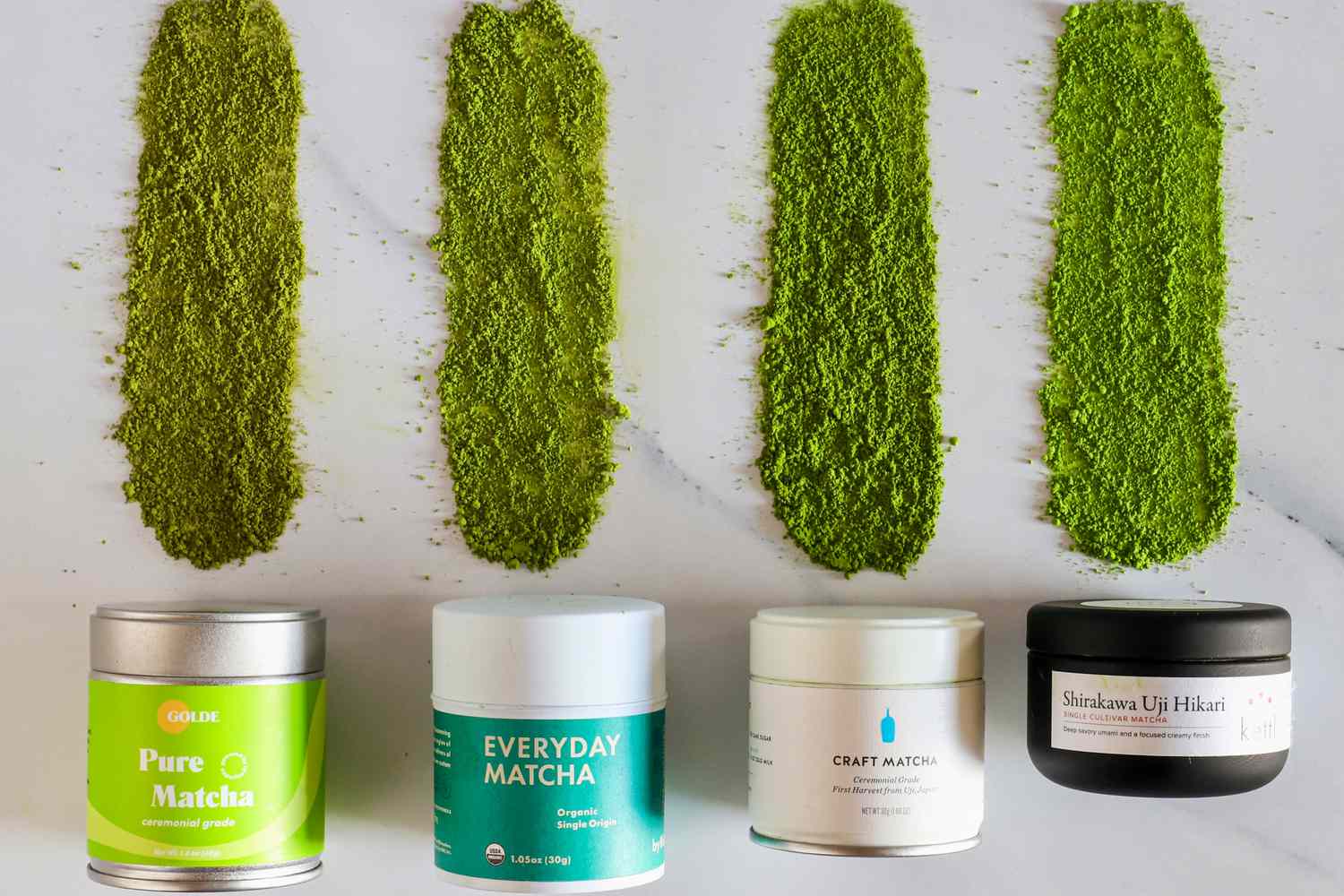 Four tins of matcha with powder beside them.