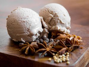 Two scoops of mulled wine ice cream displayed with whole spices: star anise allspice berries, coriander, mace