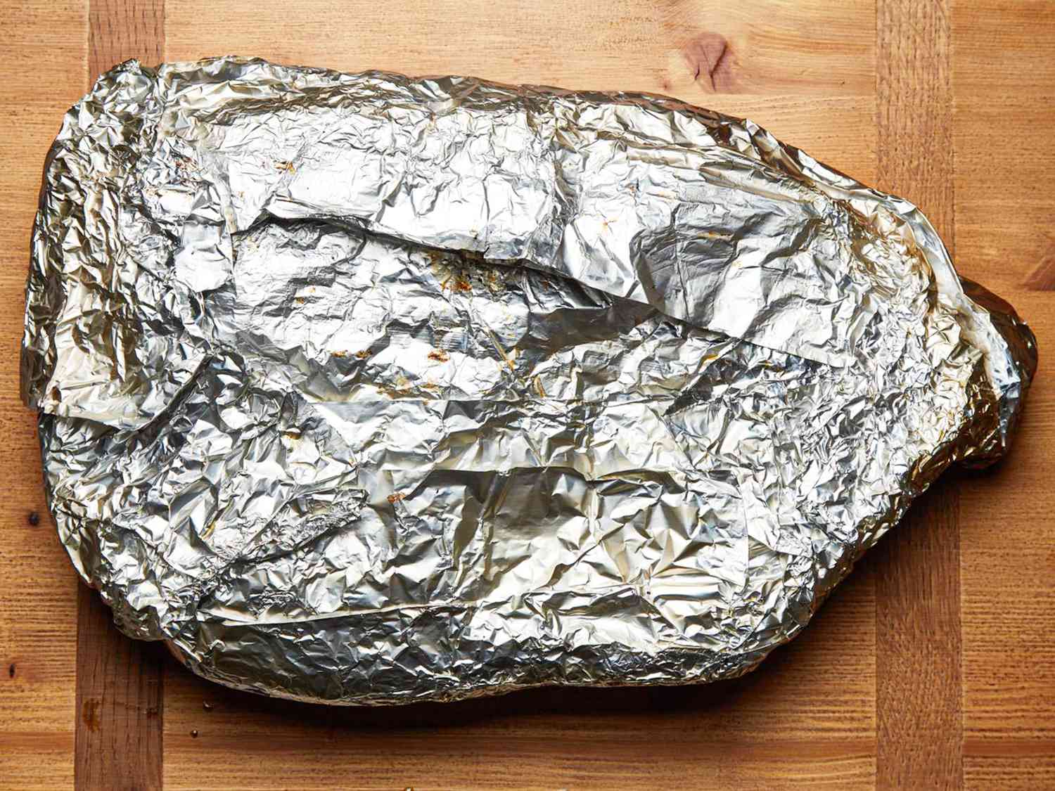 Foil-wrapped smoked brisket resting on a wooden surface