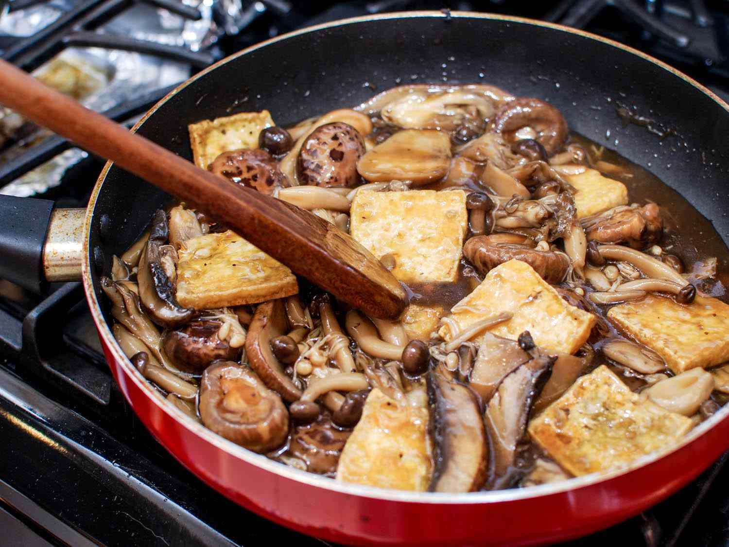 stirring together braised mushrooms and tofu in skillet