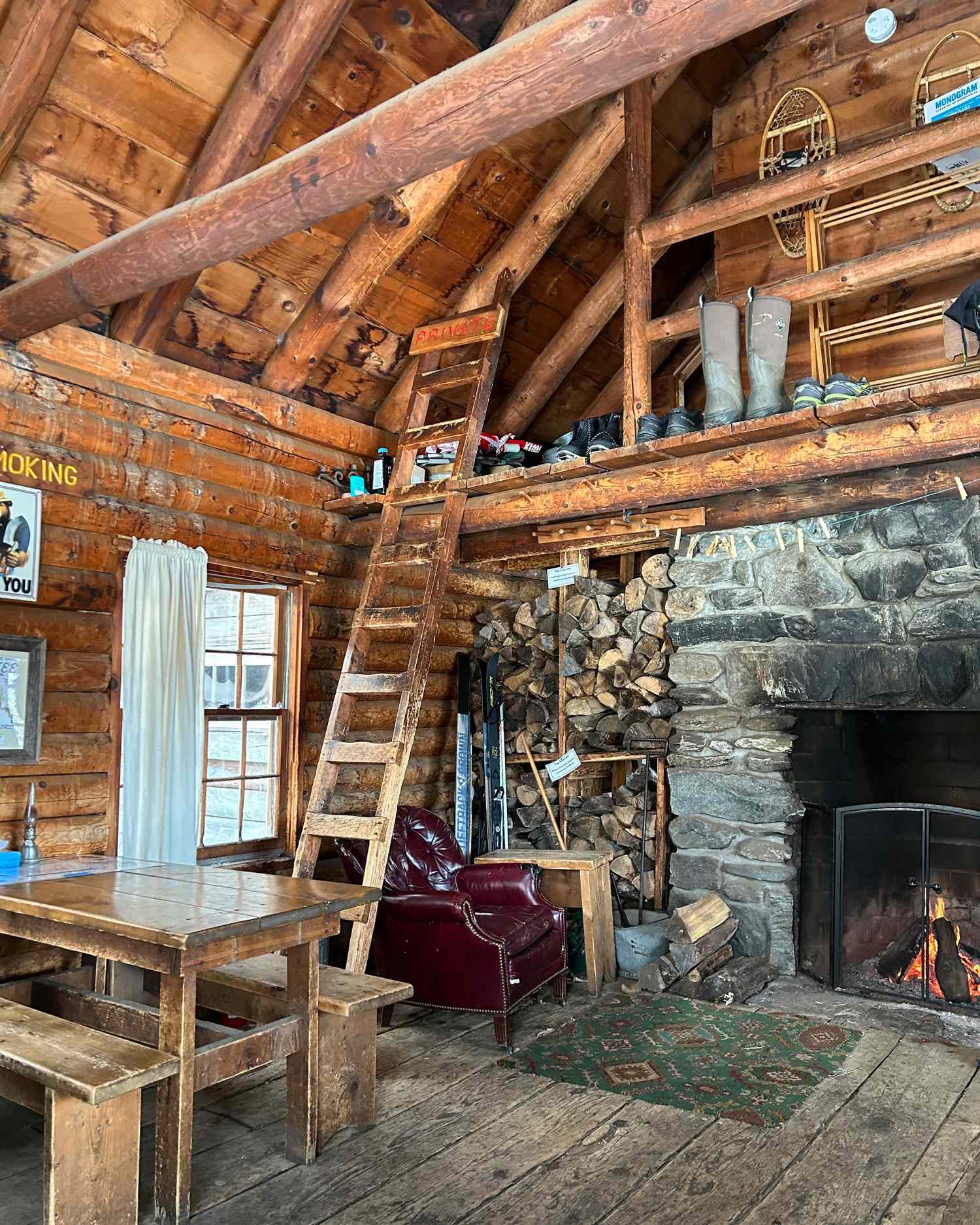 Rustic cabin interior with a stone fireplace wooden furniture and a loft accessible by a ladder