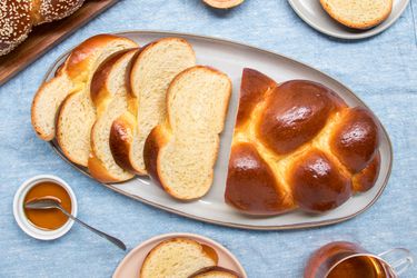 Entire loaf of plain woven challah on a plate, surrounded by smaller plates, salt, honey and a cup of tea