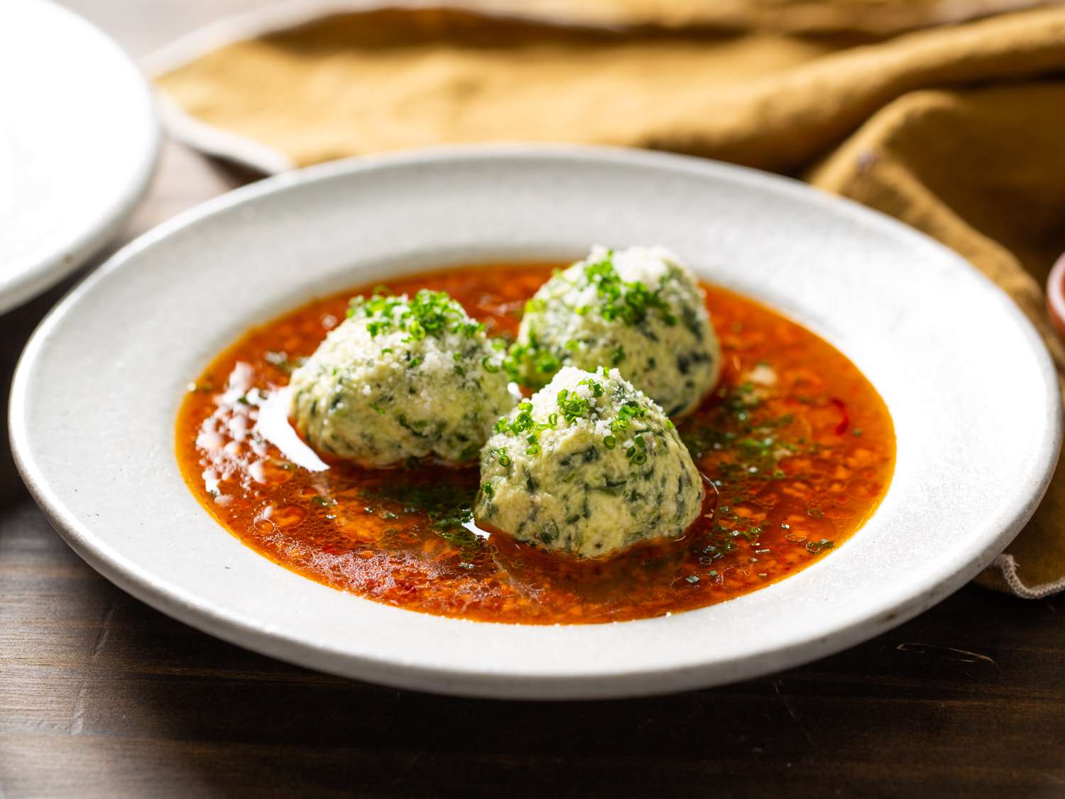 plated gnudi with broth, sprinkled with Parmesan cheese and chives