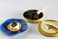 A tin of kaluga hybrid caviar next to a prepared blini topped with crème fraîche and caviar