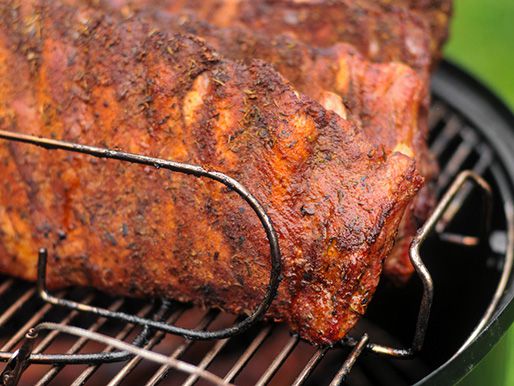 Closeup of the ribs, arranged on a rack on the grate of a smoker.