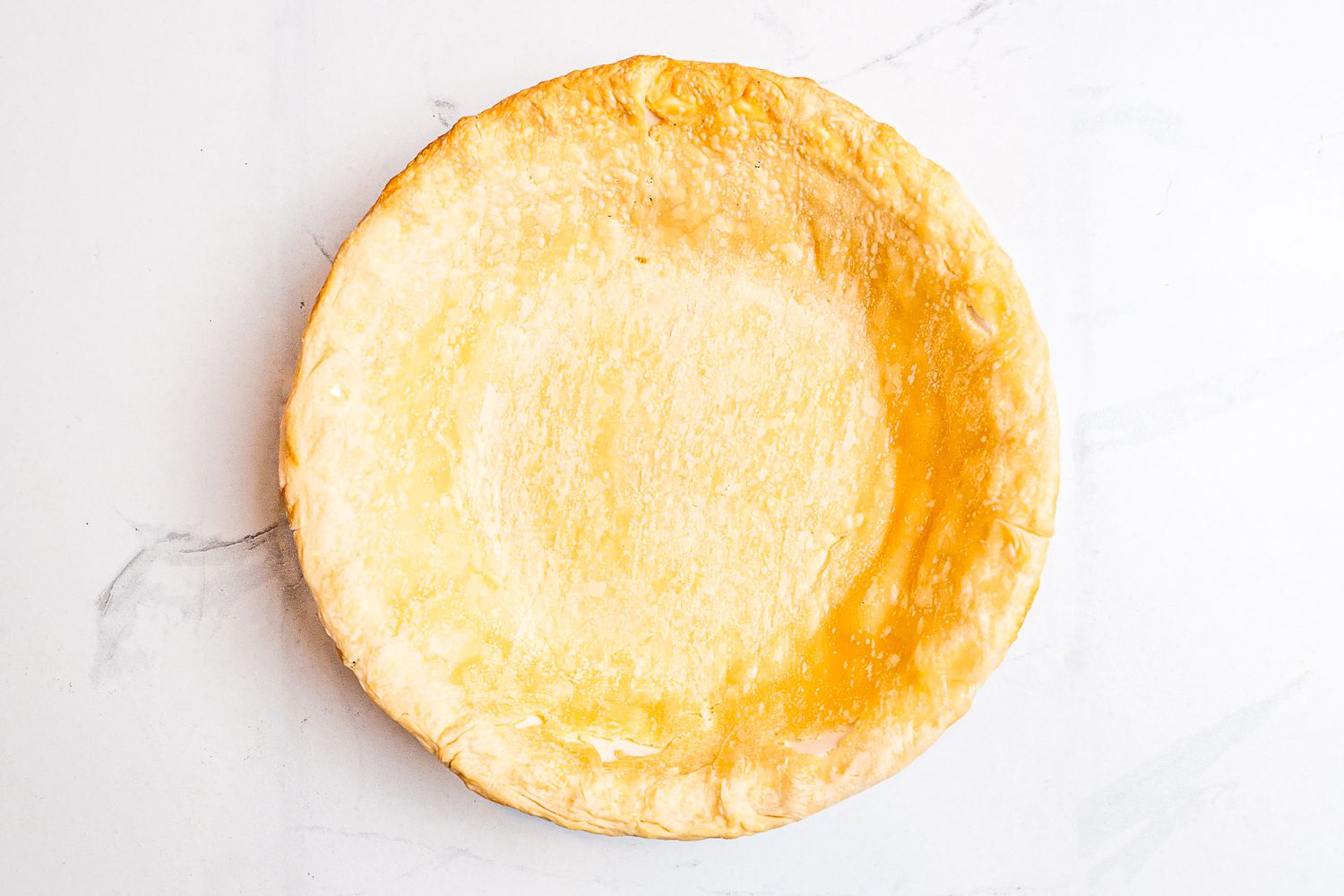 An overhead view of a baked pie crust on a marble sruface