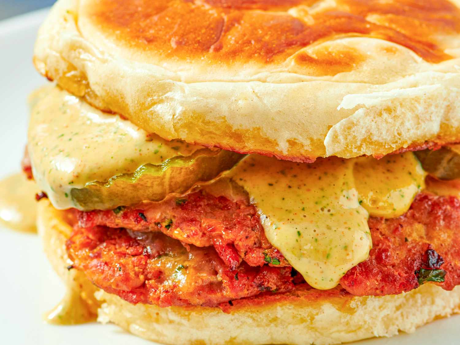 A closeup of a Turkey Chourico Smash Burger with melted sauce and pickles between buns