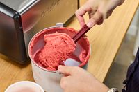 A hand using a spatula to remove ice cream from the Cuisinart Compressor Ice Cream and Gelato Maker