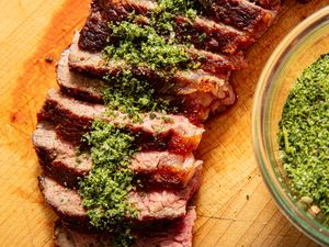 Sliced beef steak topped with herb seasoning served on a wooden cutting board