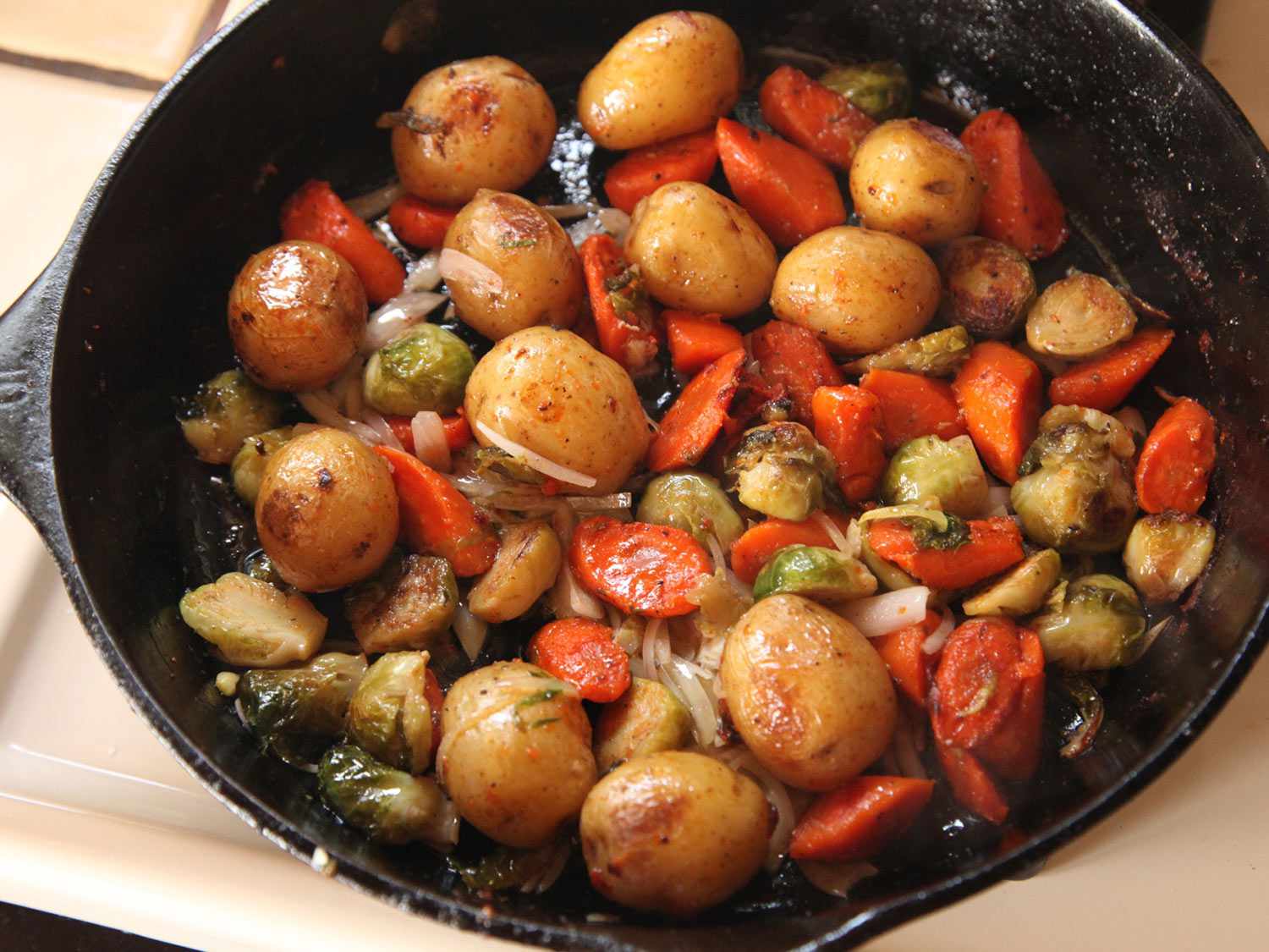 A cast iron skillet filled with roasted carrots, potatoes, and Brussels sprouts