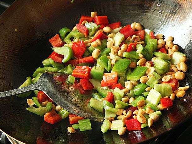 Stir-frying bell peppers, celery, and peanuts in a wok for takeout-style kung pao chicken.