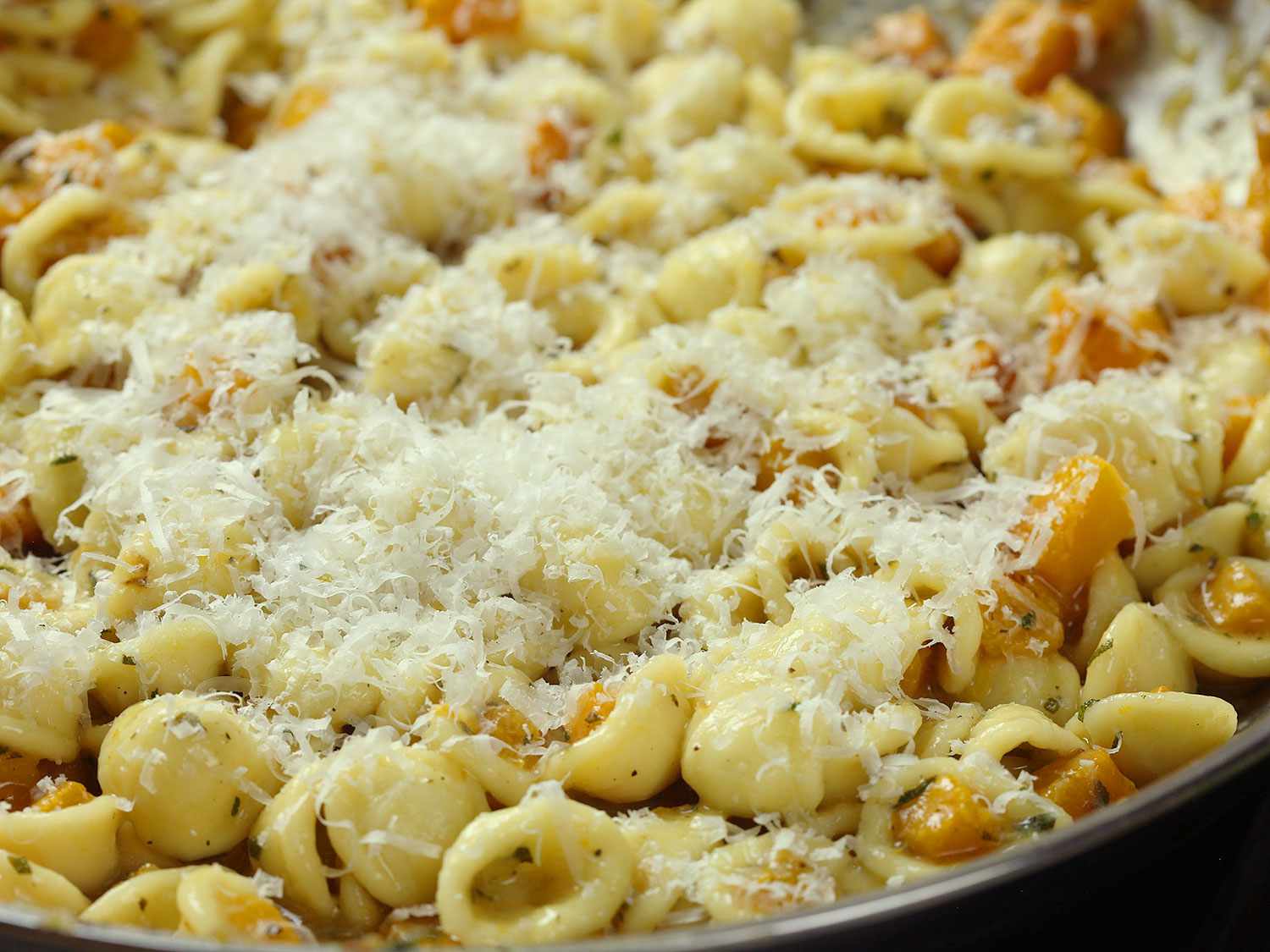 Butternut squash pasta in a skillet, covered with parmesan cheese.