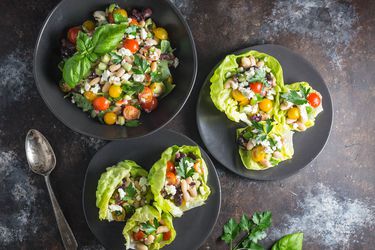 Overhead view of Quick-Marinated White Bean Salad and Feta Lettuce Cups, served on black plates next to a black bowl full of extra bean salad.
