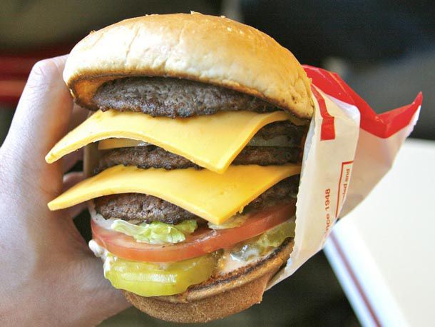 An In-N-Out burger with four patties and two pieces of cold cheese slices between each
