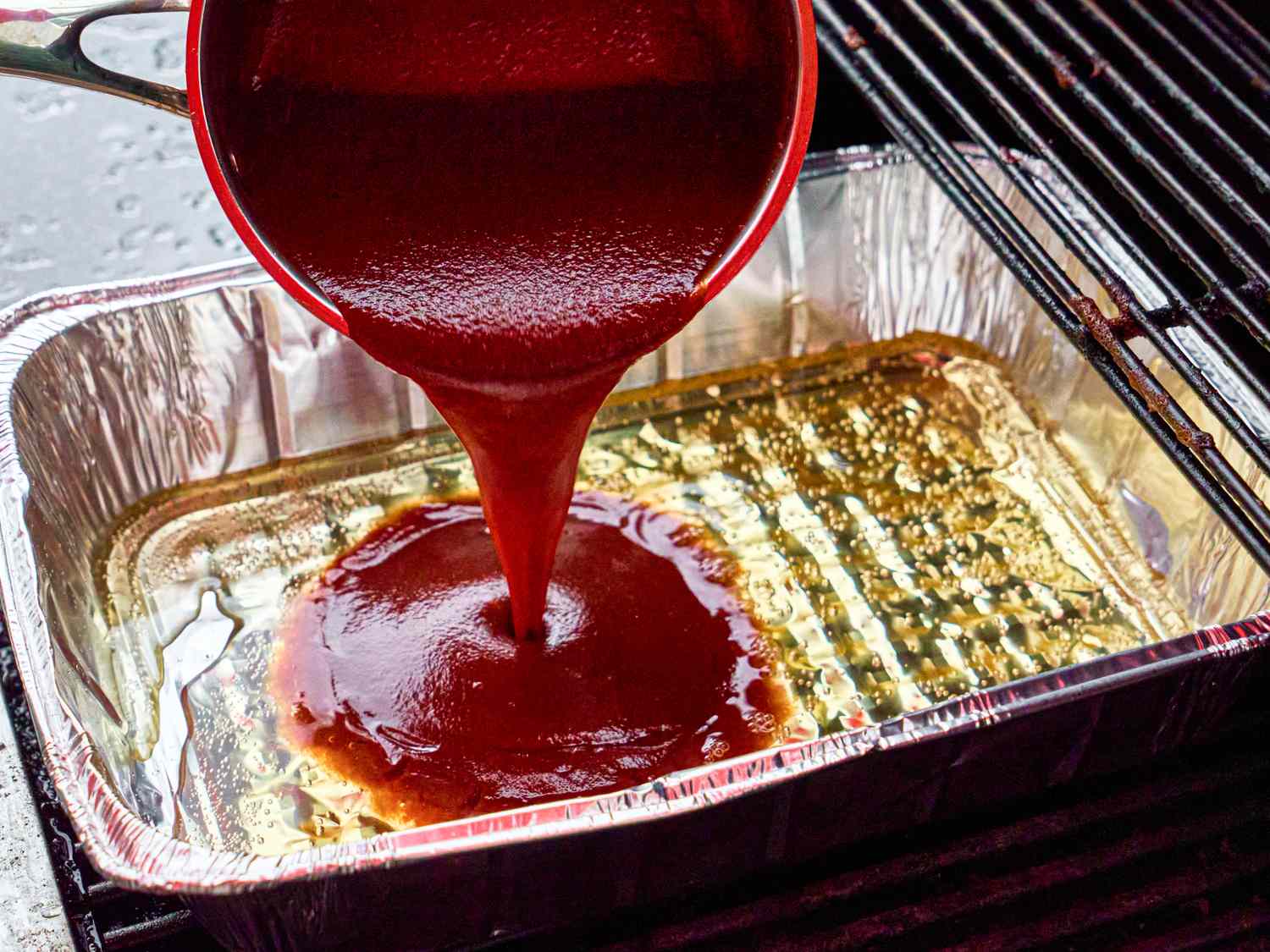 Barbecue sauce being poured into a foil tray on a grill