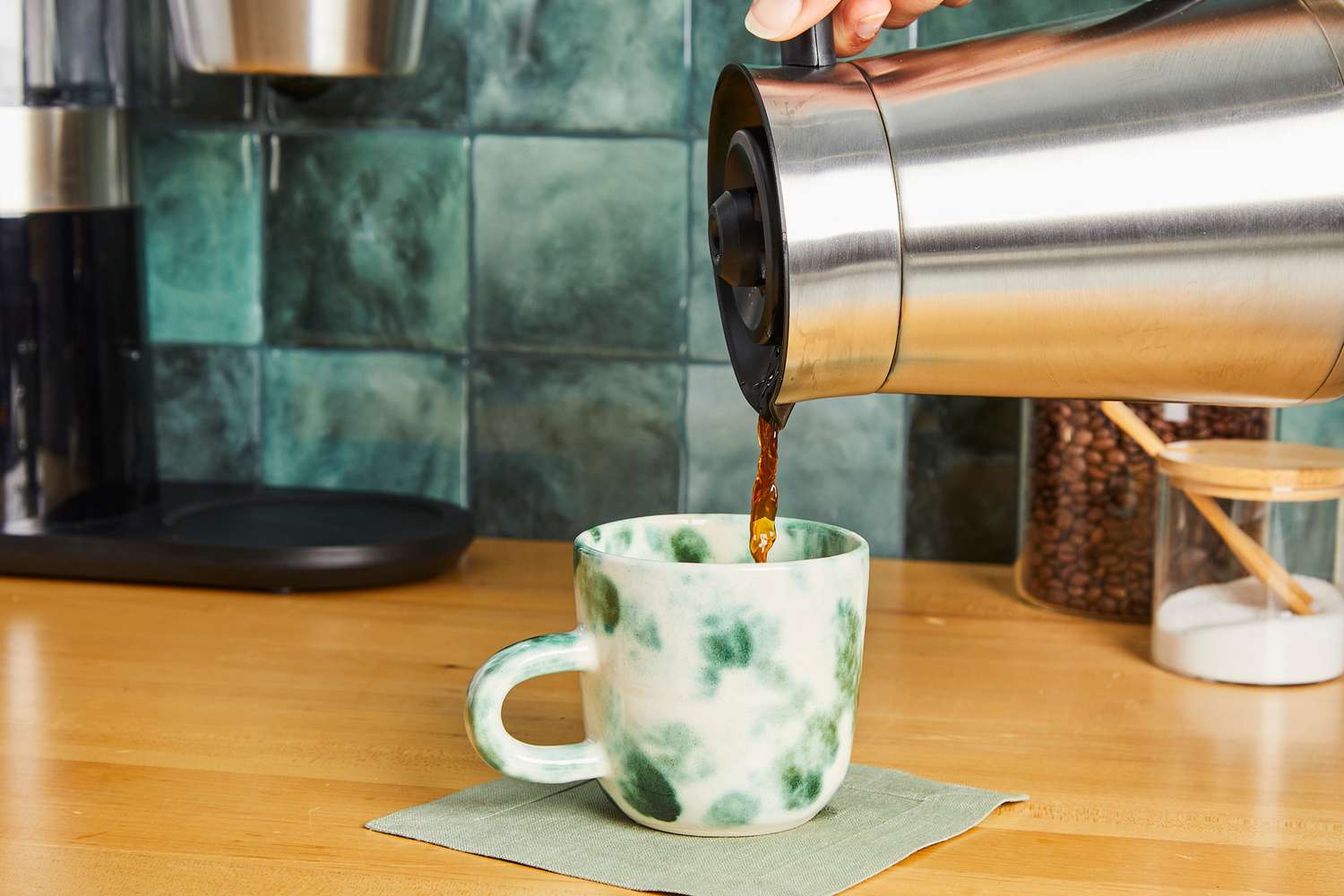 A person pouring coffee into a green and white mug.