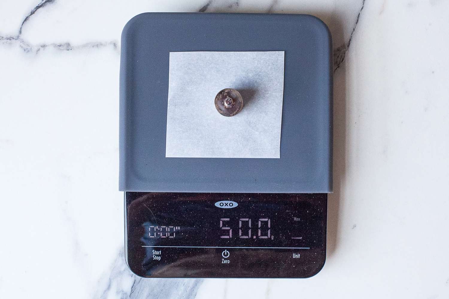 A chocolate chip on parchment paper placed on a kitchen scale reading 50 g