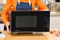 A person lifting the Magic Chef 1.1 Microwave over a wooden counter