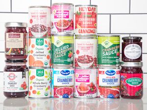 An assortment of canned and jarred cranberry sauces displayed on a counter in a tiled background setting