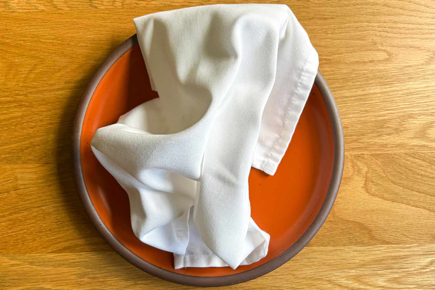 A folded cloth napkin on an orange ceramic plate
